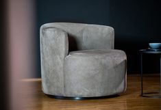 a grey chair sitting on top of a wooden floor next to a table and lamp