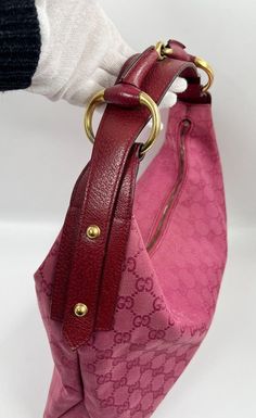 A Vintage Gucci Hobo made from pink canvas with the GG monogram. Red leather trim with gold hardware. Iconic bit hardware detail on the shoulder strap. The inside of the bag features an interior zipped pocket for valuables. This bag is in good vintage condition with some minor wear to be seen to the canvas and base corners. Inside there is the serial number on the back of the leather Gucci tab inside. Height: 25cm Depth: 35cm Width: 9cm Gucci Hobo Bag, Gg Monogram, Pink Canvas, Diaper Backpack, Vuitton Bag, Leather Trim, Hobo Bag, Vintage Gucci, Leather Trims