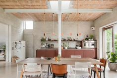 an open kitchen and dining room area with wooden ceiling beams, exposed brick walls, white painted flooring and large windows