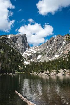 the mountains are covered in snow and trees near a body of water with a log sticking out of it