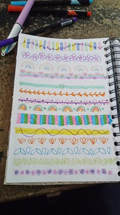 an open notebook with colorful doodles and markers on it next to colored pencils