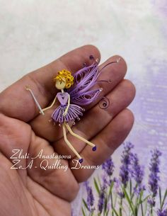 a hand holding a tiny purple fairy figurine