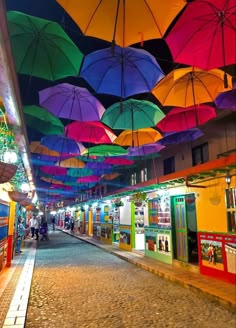 many colorful umbrellas hanging from the ceiling above a street