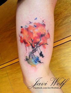 a watercolor tree tattoo on the left leg with birds flying around it and an orange sky