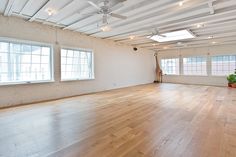 an empty room with wooden floors and white walls, exposed ceiling fan and windows in the corner