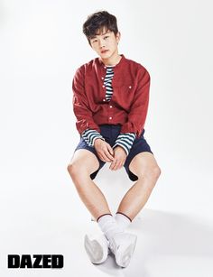 a young man sitting on top of a white chair wearing shorts and a red cardigan