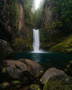 a large waterfall in the middle of a forest with moss growing on it's sides