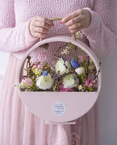 a woman in a pink dress holding a basket with white and pink flowers on it