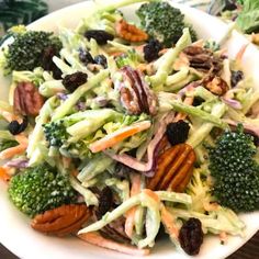 a salad with broccoli, carrots and pecans on a white plate