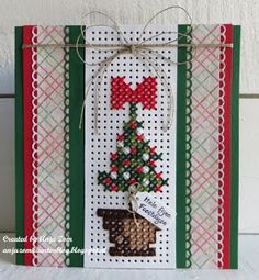 a cross stitch christmas card with a small tree on the front and red ribbon hanging from it