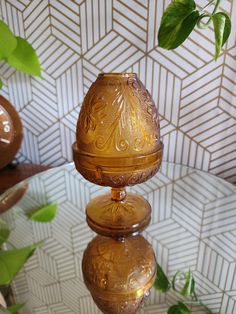 two golden vases sitting on top of a glass table next to a potted plant