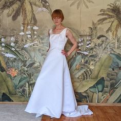 a woman is standing in front of a wall with palm trees and birds on it