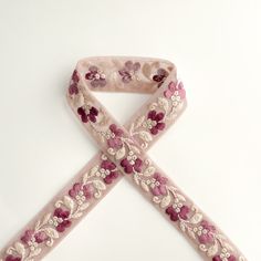 a pink ribbon with flowers and pearls on the end is sitting on a white surface