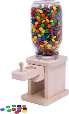 a jar filled with lots of candy sitting on top of a wooden stand next to several different colored candies