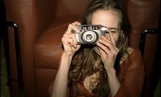 a woman sitting in a chair holding up a camera