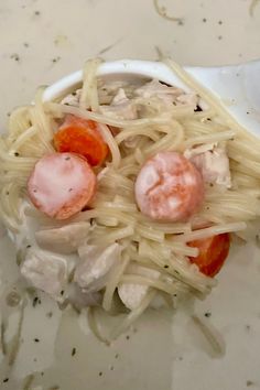 some noodles with meat and tomatoes in a white bowl on a table next to a spoon