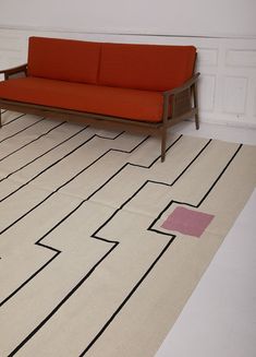 a red couch sitting on top of a white floor next to a rug with black lines