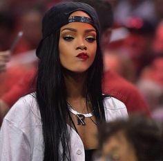 a woman with long black hair and red lipstick wearing a beanie at a basketball game