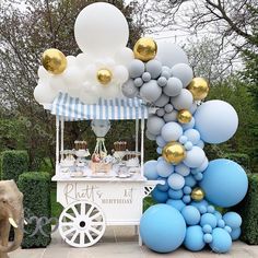 an elephant is standing next to a cart with balloons on it and a cake stand in the background