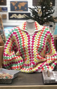 a crocheted sweater sits on a table next to a christmas tree and other items