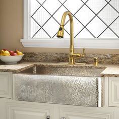 a kitchen sink sitting under a window next to a bowl of fruit