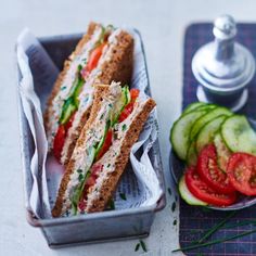 a sandwich in a tin next to some sliced cucumbers