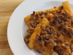 a white plate topped with macaroni and cheese covered in ground beef on top of a wooden table