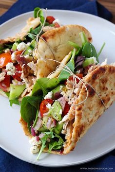 two pita sandwiches on a white plate with lettuce, tomato and feta cheese