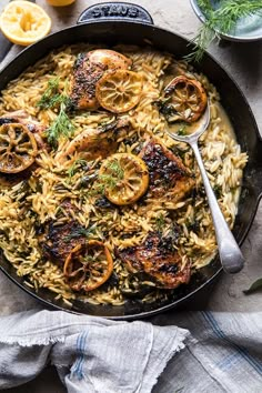 a skillet filled with chicken and rice covered in lemons, herbs and spices