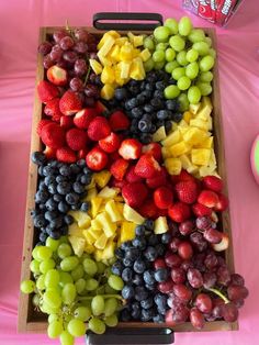 a wooden tray filled with grapes, strawberries and other fruit on a pink table cloth