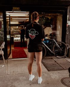 a woman standing on the sidewalk in front of a building with a bike parked next to her