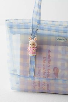 a small teddy bear in a pink dress on a blue and white checkered tote bag