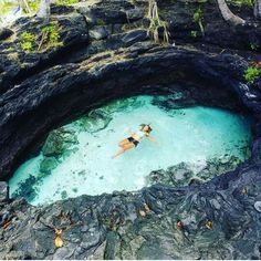 a woman swimming in the blue lagoon on an island with black rocks and green vegetation