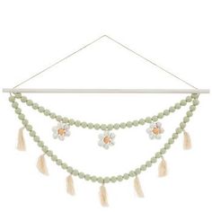 a green beaded necklace with flowers and tassels hanging from a white wall