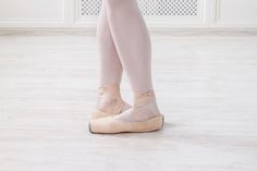 a ballerina's feet in ballet shoes on a white floor with a wall behind them