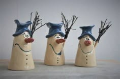 three ceramic snowmen with hats and noses on their heads, one is holding branches