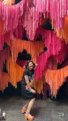 a woman standing in front of a wall covered with pink, orange and yellow streamers