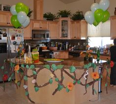 balloons are hanging from the ceiling above a kitchen island decorated with branches and flowers,