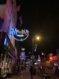 people are walking down the street in front of neon signs and buildings at night time