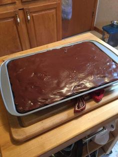 a large chocolate cake sitting on top of a wooden counter next to a pan filled with frosting