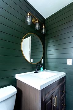 a white toilet sitting next to a bathroom sink under a round mirror on a green wall