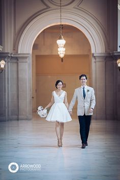 a man and woman are walking through an archway holding hands while dressed in white dresses