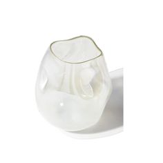 a white glass vase sitting on top of a white plate with a spoon in it