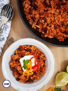 two bowls filled with chili and meat next to limes on the side, along with a fork