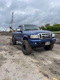 a blue pick up truck parked on top of a dirt covered field next to a crane