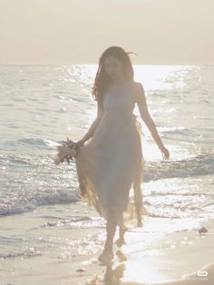 a woman in a white dress is walking on the beach