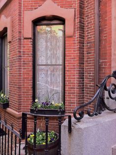 an iron railing and window on the side of a red brick building with potted plants