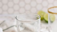 two glasses filled with water sitting on top of a table next to limes and a knife