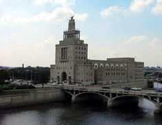 a large building sitting on top of a river next to a bridge with cars driving across it