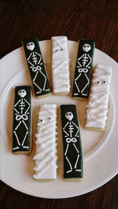 four decorated cookies on a plate with black icing and white icing in the shape of skeletons